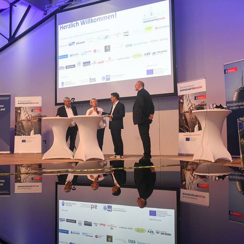 Vier Begrüßungsredner:innen auf der Bühne im Gespräch