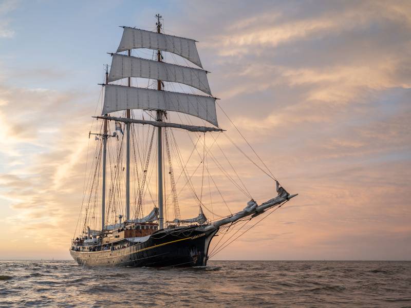 Segelschiff Gulden Leeuw auf dem Meer bei Sonnenuntergang. Abgebildet ist ein altes Segelschiff auf dunklem Wasser.